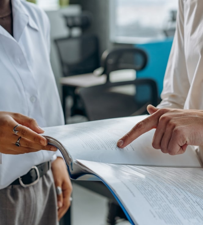 Man pointing to a document and discussing it with a woman wearing white shirt in an office