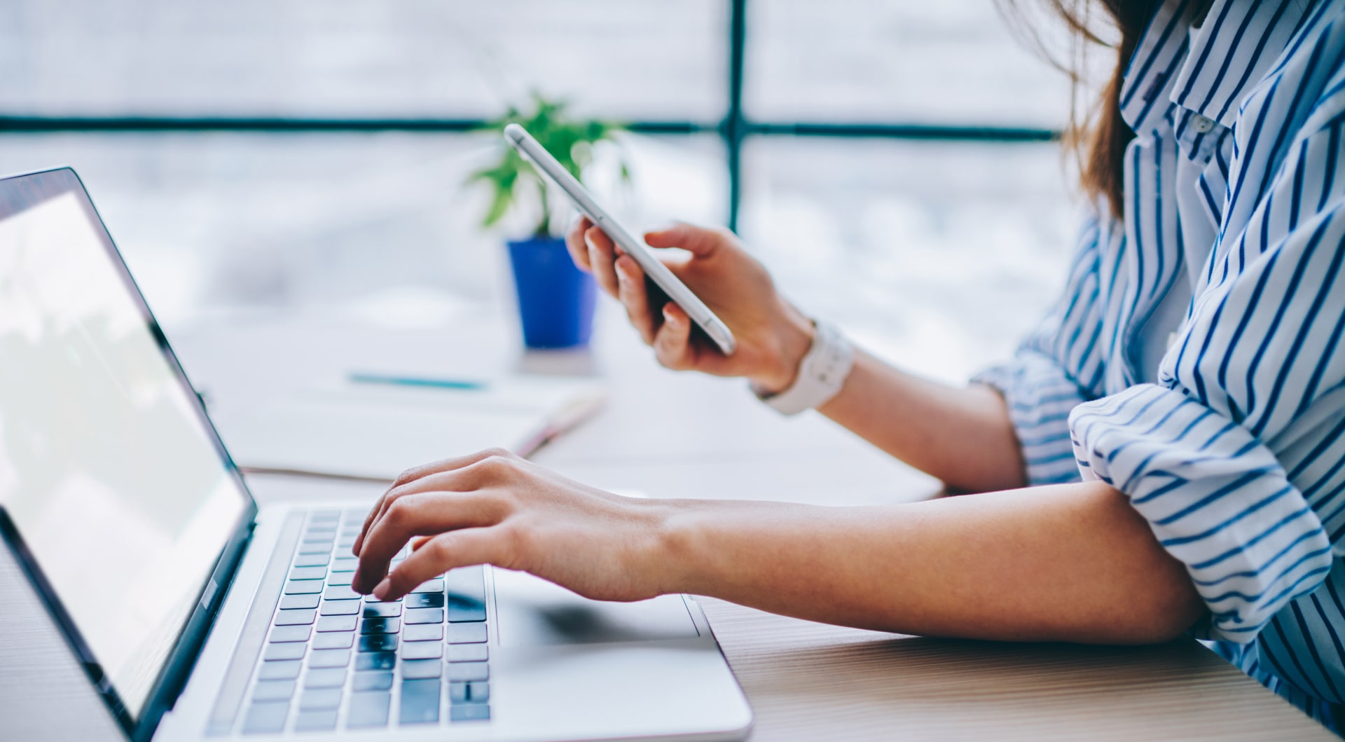 Lady at computer holding phone office desk notebook in background blur